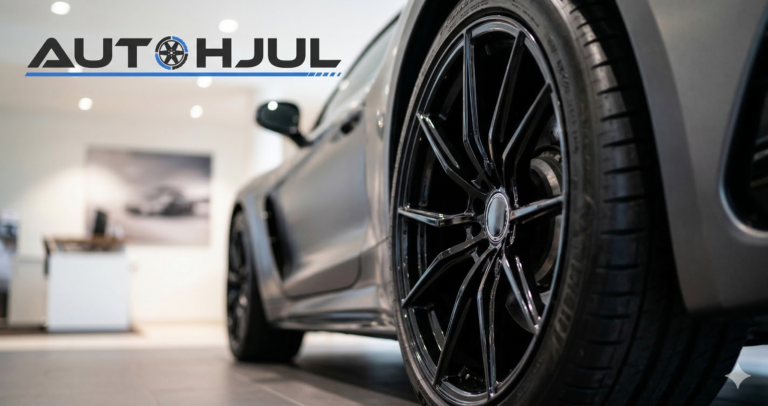 Närbild på en modern mörk fälg och ett däck monterat på en sportbil med Autohjul.se logotyp i verkstadsmiljö.